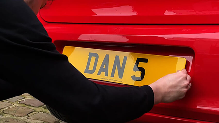 A man mounting a new private number plate on the rear of a car